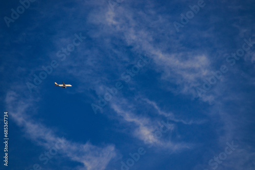 side view of a commercial jet airliner, flying under a blue sky covered by a veil of thin white clouds.