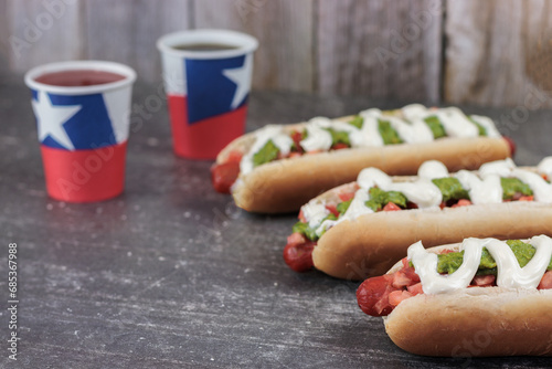 Completo Italiano Chileno: hot dog bun with vianesa, tomato, palta and mayo with poly paper cups chilean flag on chilean national holidays. on cement table. Typical Chilean food concept