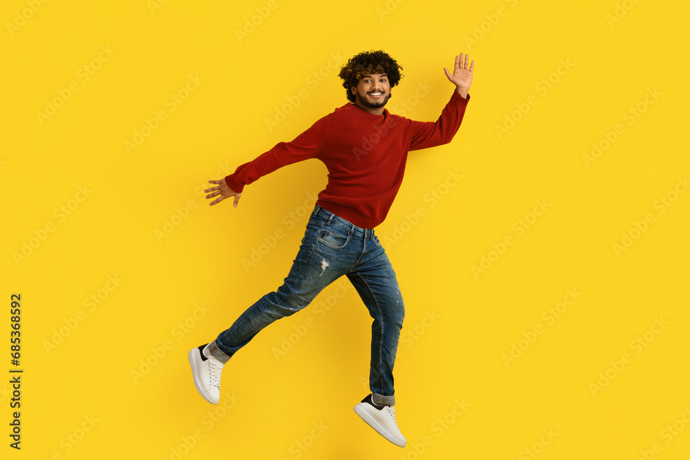 Excited young indian guy jumping over yellow background