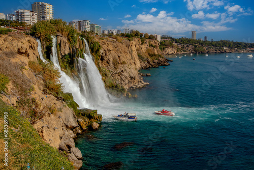 The moment when the Lower Düden waterfall flows into the sea, against the background of the steep shores of the Mediterranean and the urban development of the city of Antalya.