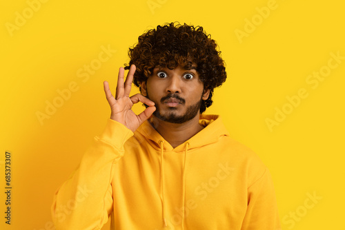 Quadro em tela Handsome indian guy zipping his mouth on yellow background