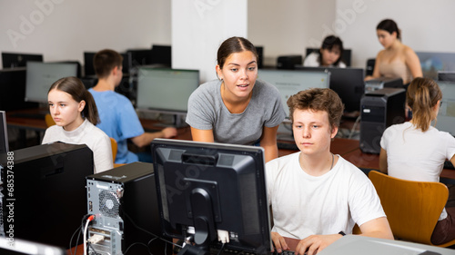 Young female teacher working with schoolboy in computer class of school library