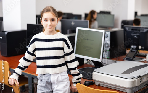 Portrait of diligent smiling teen schoolgirl standing in computer class ready for lesson. Modern education for children concept