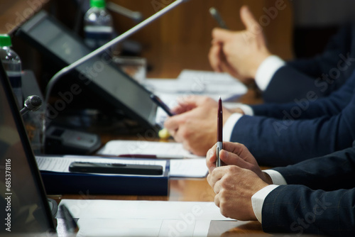 Hands of an important man - a politician, deputy, businessman or lawyer, sitting at a table with a pen, documents and monitors. Negotiations, meeting or conference. Photo. Selective focus