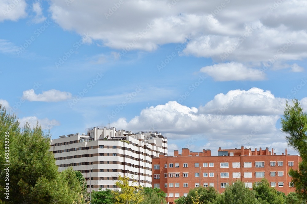 Modern buildings seen through vivid greenery under cloudy vibrant sky in Madrid, Spain