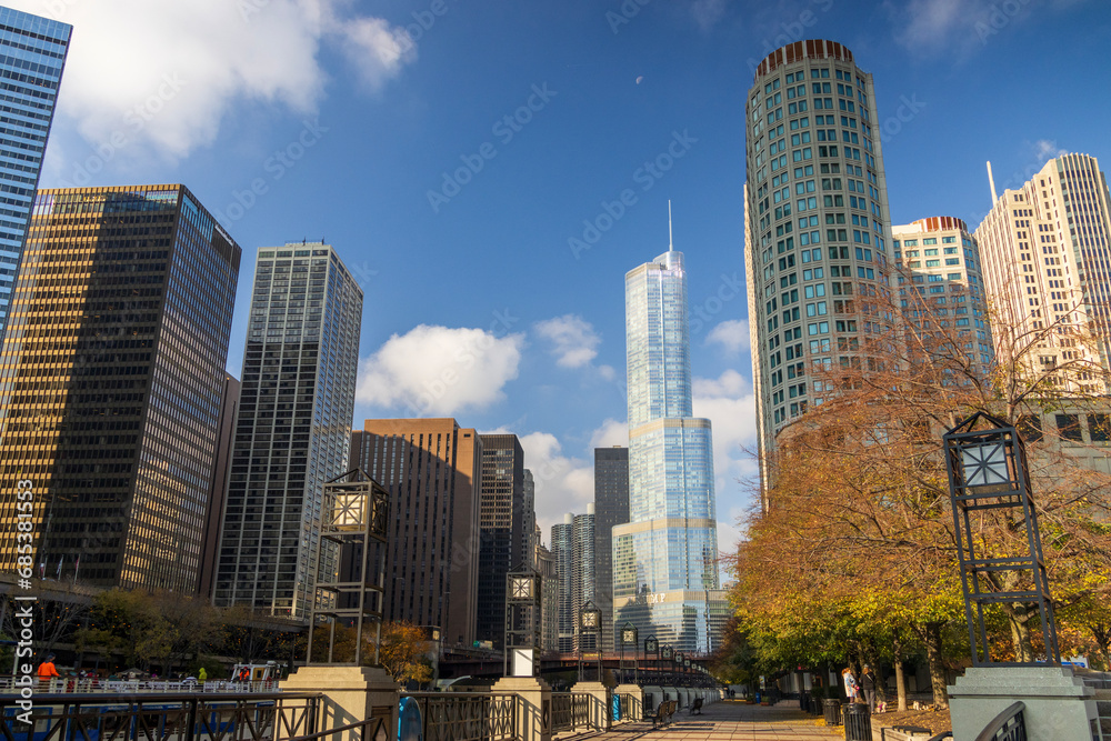 Obraz premium A beautiful autumn landscape along the Chicago River with skyscrapers, hotels and office buildings in the city skyline, autumn trees, blue sky and cloud in Chicago Illinois USA