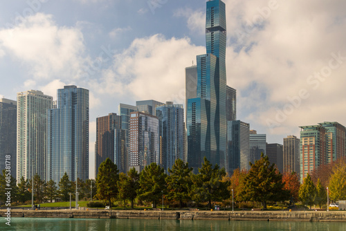 A beautiful autumn landscape along Lake Michigan with skyscrapers, hotels and office buildings in the city skyline, green water and autumn trees, blue sky and clouds in Chicago Illinois USA