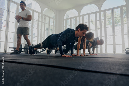 Trainer applauding group of multiracial young adults in sports clothing doing push-ups at the gym