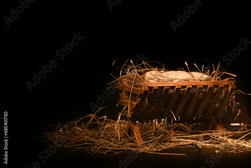 Tableau sur toile Manger with baby and hay on wooden table against dark background