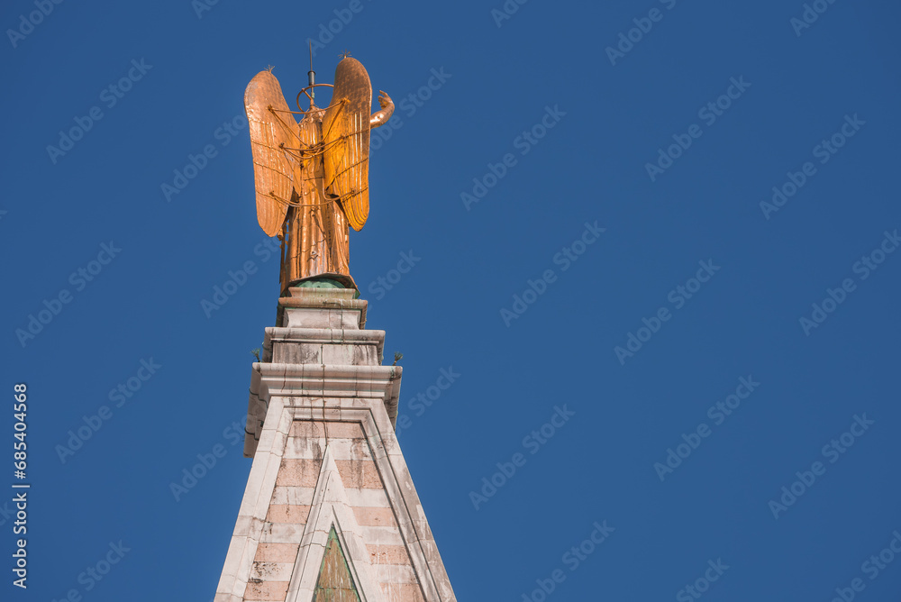 Fototapeta premium A stunning angel statue adorns a building in Venice, Italy. The photo captures a beautiful architectural element, adding to the charm and historical significance of the city.