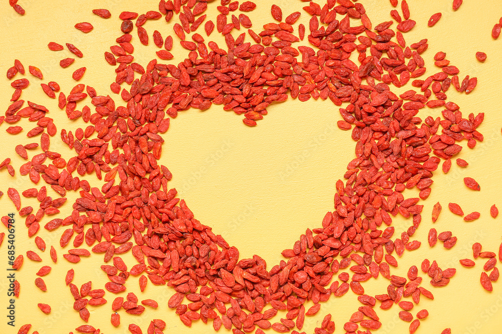 Heart made of red dried goji berries on yellow background