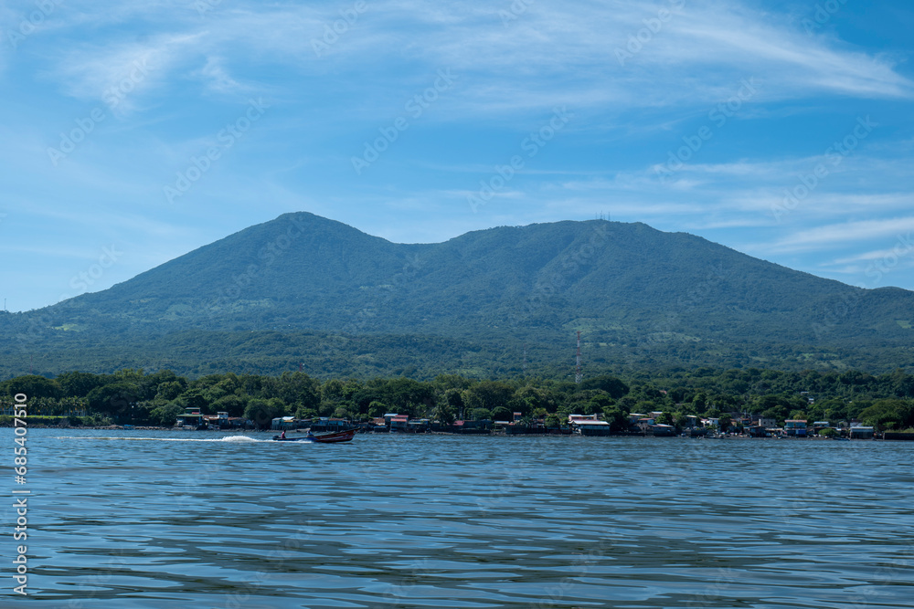 Coastline Seen From Afar with a Volcanic Mountain, Lush Vegetation Forest, Beach, Houses and a Speed Boat on a Calm Ocean