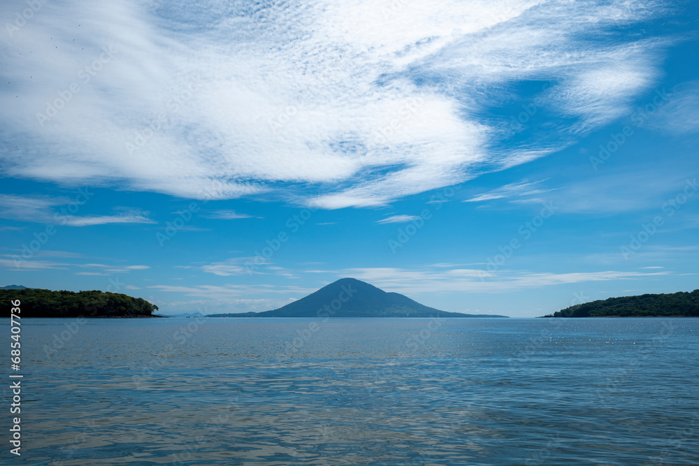 Beautiful Volcanic Island Seen From Afar Between Two Other Islands with Volcanic Hills, Patches for Grazing and Forest in Front of a Calm Ocean with Birds and Boats Beautiful Volcanic Island Seen From Afar Between Two Other Islands with Volcanic Hills, Patches for Grazing and Forest in Front of a Calm Ocean with Birds and Boats