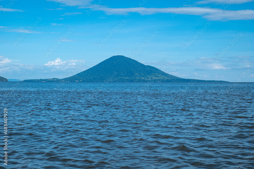 Volcanic Mountain with Lush Vegetation Forest in Front of a Calm Blue Ocean