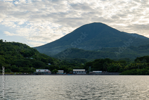 Obraz na płótnie Coastline Seen From Afar with a Volcanic Mountain, Lush Vegetation Forest, Beach, and Houses with a Calm Ocean w salonie