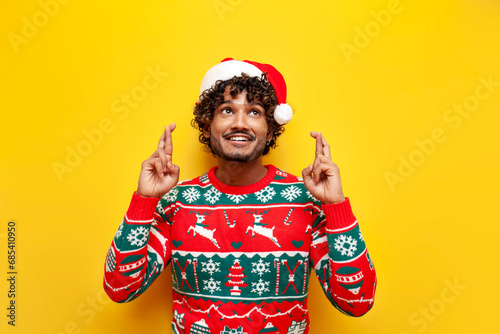 young indian man in new year clothes waiting and hoping with fingers crossed on yellow isolated background