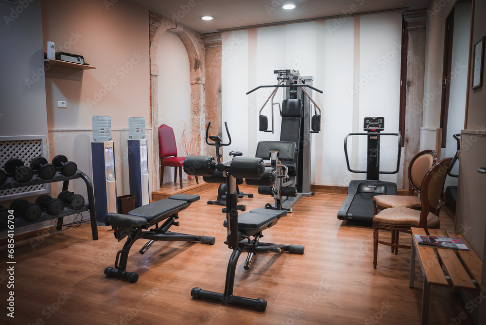 Modern gym room with exercise equipment including a rowing machine, captured from a side angle. No flooring or windows are visible. - obrazy, fototapety, plakaty 
