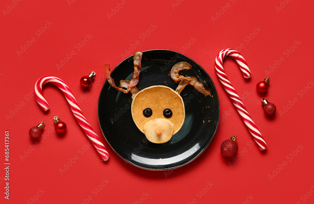 Plate with pancake in shape of reindeer on red background. Christmas celebration - obrazy, fototapety, plakaty 