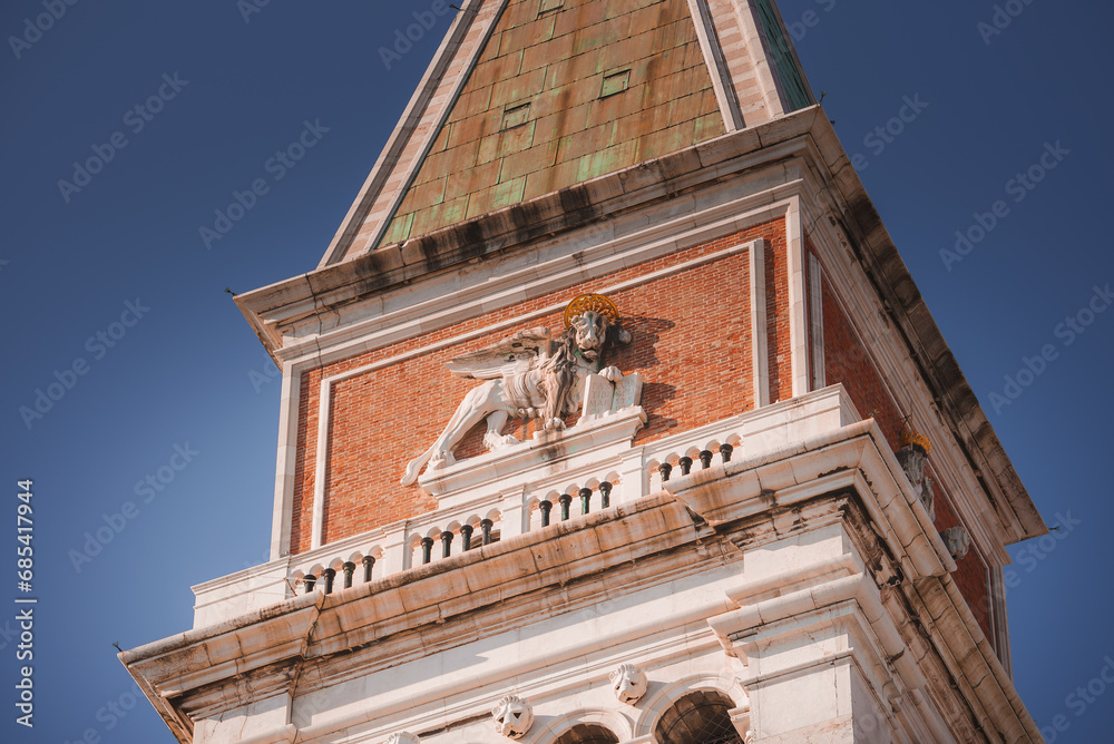 Fototapeta premium A majestic clock tower with a lion statue on top, set against a clear sky. The architectural style and location are unknown.