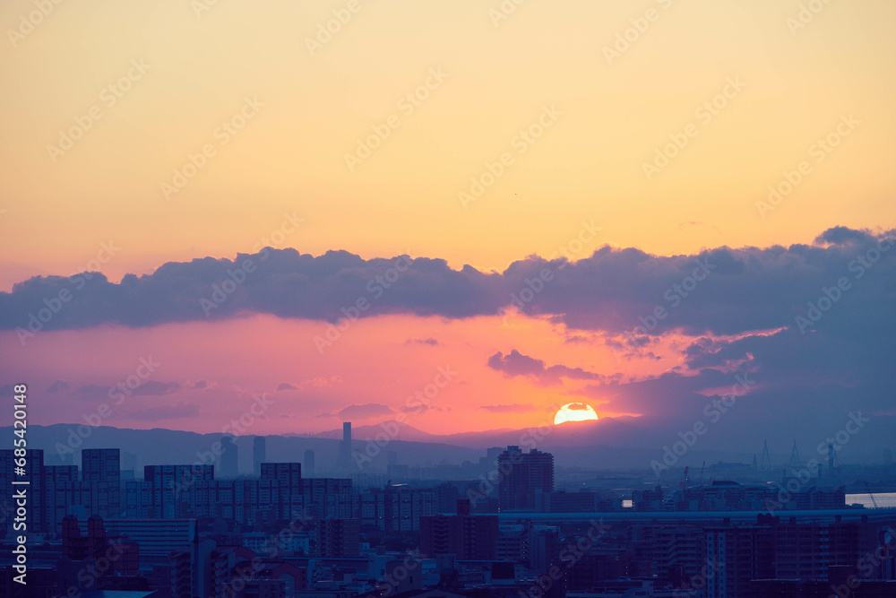 都市の夜明け。神戸市の高台から大阪湾と大阪南港から朝日が昇る。雲の隙間から天使の梯子。