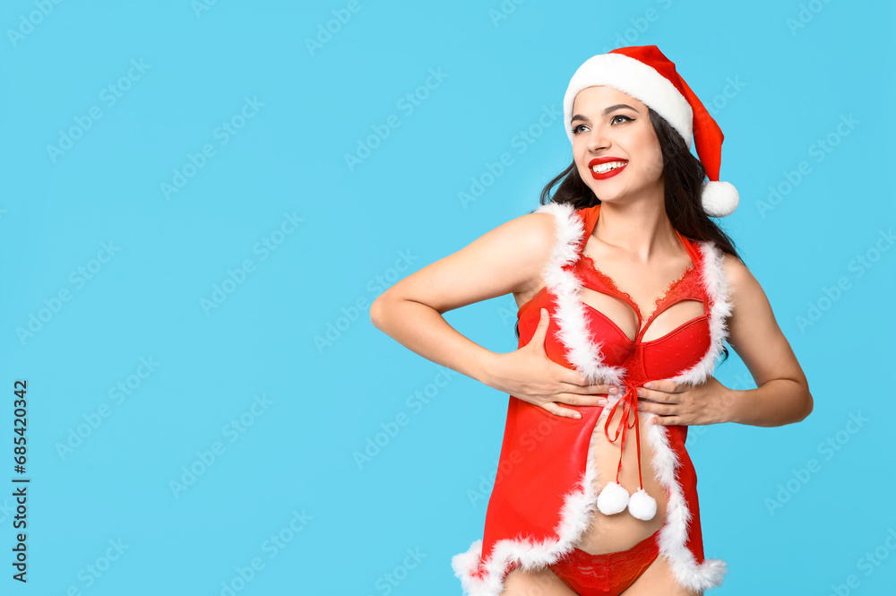 Obraz premium Beautiful young sexy woman in lingerie and Santa hat on blue background