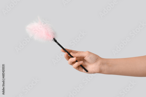 Female hand with feather stick from sex shop on grey background, closeup