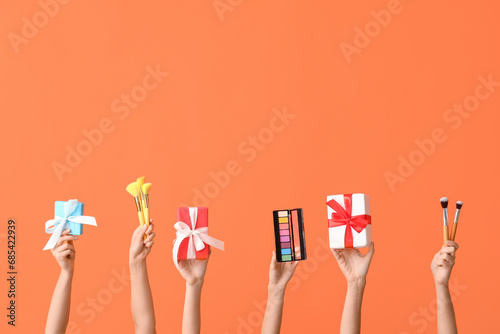 Female hands with different cosmetic products and gifts on orange background
