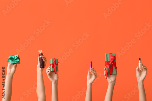Female hands with different cosmetic products and gifts on orange background