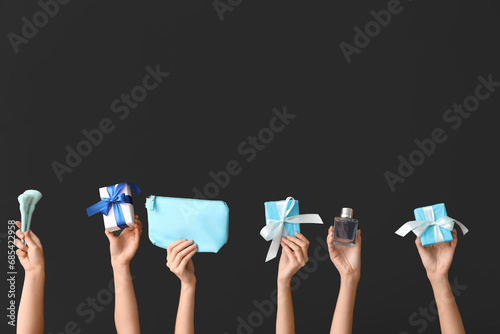 Female hands with different cosmetic items and gifts on black background