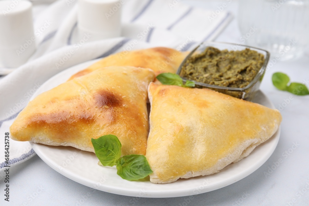 Delicious samosas with basil and pesto sauce on white table, closeup