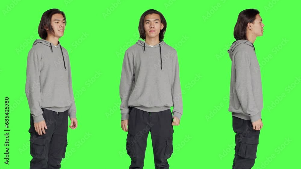 Asian friendly model standing in studio and posing with confidence, smiling against isolated greenscreen background. Young adult acting optimistic and relaxed in casual jeans. Asian friendly model standing in studio and posing with confidence, smiling against isolated greenscreen background. Young adult acting optimistic and relaxed in casual jeans.