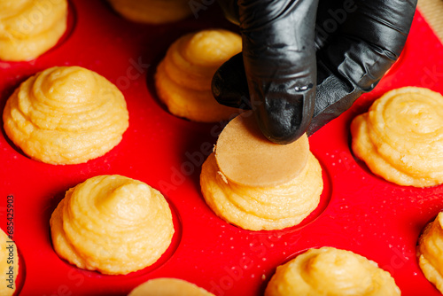 In the kitchen showing the process of placing craquelin on the top of choux pastry prior to baking.  photo