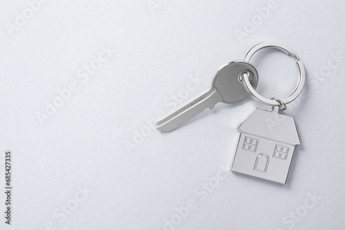 Key with keychain in shape of house on light background, top view. Space for text