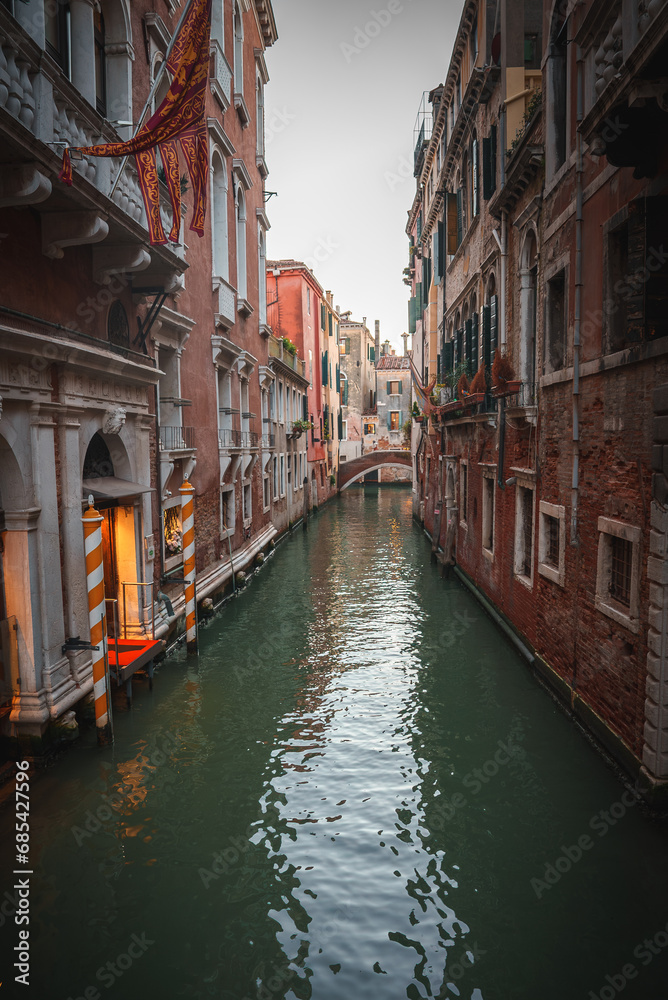Explore the charm of Venice, Italy with this serene image capturing a narrow canal. The tranquil beauty of the architecture and water creates a picturesque scene.