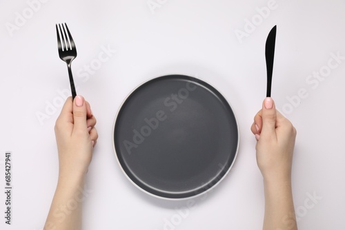 Woman holding fork and knife near empty plate at white table, top view