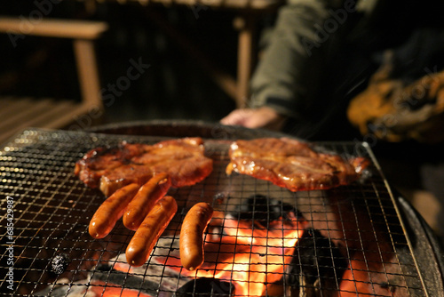A glowing camp fire providing comfortable lights and barbecue grill pit with glowing and flaming of fire with hot charcoal briquettes with night time outdoor background