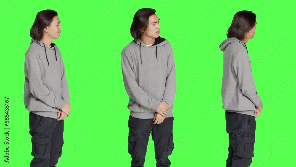 Young male model looks at watch standing against greenscreen backdrop, acting impatient in studio. Asian person feeling frustrated and irritated, waiting for a certain something. Young male model looks at watch standing against greenscreen backdrop, acting impatient in studio. Asian person feeling frustrated and irritated, waiting for a certain something.
