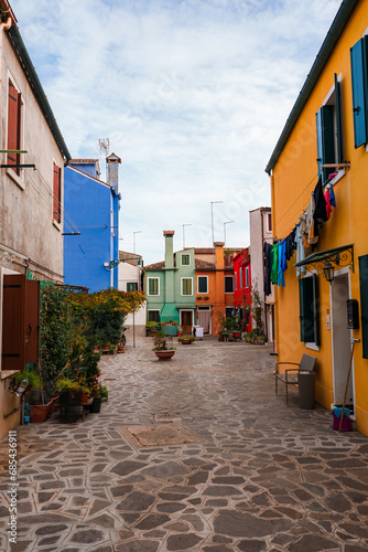 Explore the charming and picturesque streets of Burano, Italy. Vibrant, colorful buildings line the narrow cobblestone street, capturing the essence of Venetian charm and local culture.