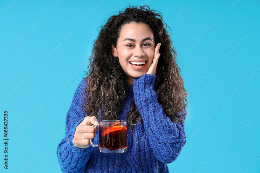 Happy young African-American woman with glass cup of hot mulled wine on blue background Happy young African-American woman with glass cup of hot mulled wine on blue background