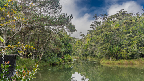 The river flows calmly in a tropical rain forest. Circles on the water. Lush green vegetation on the banks. Blue sky  clouds. Madagascar. Vakona Forest Reserve. 