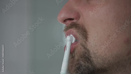 Man brushes his teeth with an electrical tootbrush at morning bathroom before work. Male uses an electric sonic dental cleaning brush. Daily dental hygiene and oral health with eletrical teethbrush.  photo