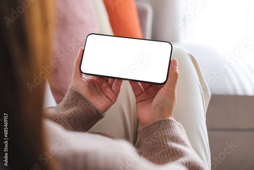 Mockup image of a woman holding mobile phone with blank desktop white screen while sitting on a sofa at home © Farknot Architect