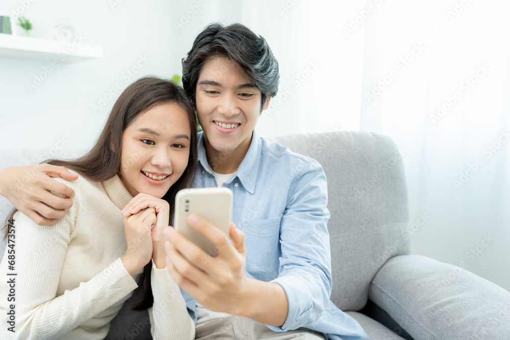 Asian couple smiling and happily use smartphone to online shopping. Husband ready to pay birthday present for beautiful wife. Find accommodation online for honeymoon, App online, book flight tickets. Asian couple smiling and happily use smartphone to online shopping. Husband ready to pay birthday present for beautiful wife. Find accommodation online for honeymoon, App online, book flight tickets.