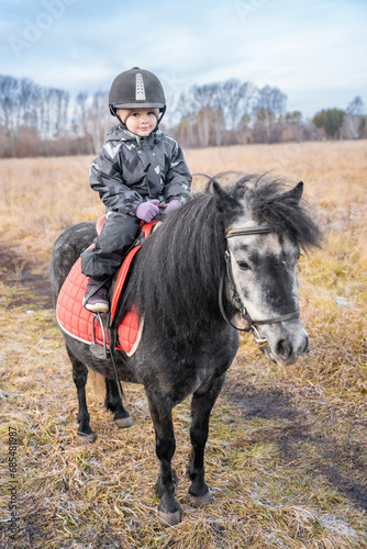 Little girl riding a little horse or pony in the winter in field in the winter © dtatiana