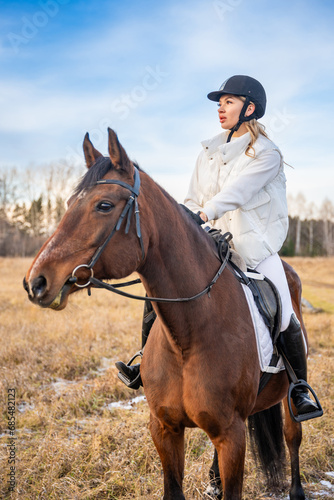 Beautiful professional female jockey riding a horse in field in winter