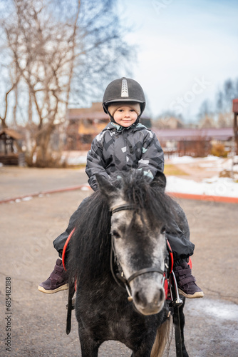 Cute little girl riding a little horse or pony in the winter on farm
