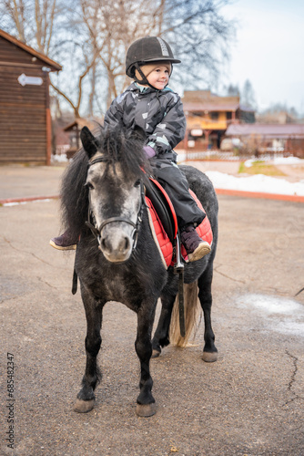 Cute little girl riding a little horse or pony in winter on farm