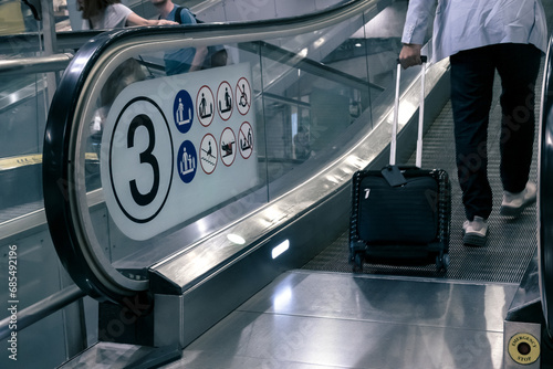 tourist with travel luggage steps on travelator, tread or moving walkway in airport terminal, emergency stop button photo