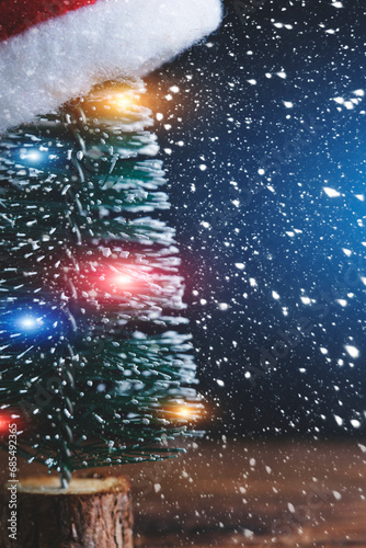 Christmas tree with garland is decorated with Santa Claus hat background falling snow.