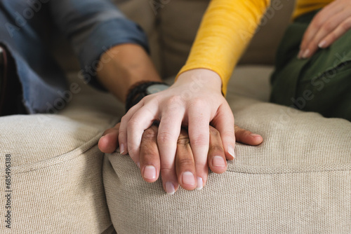 Diverse couple sitting on couch and holding hands in living room at home, copy space © WavebreakMediaMicro
